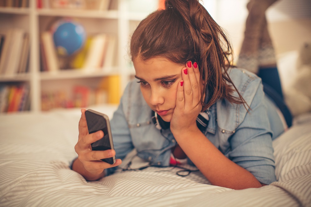 Ein Maedchen schaut gelangweilt auf ein Smartphone