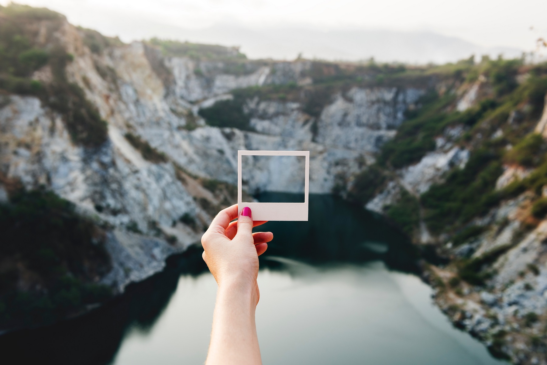 Eine Hand hält einen Polaroid-Rahmen vor eine Bergkulisse