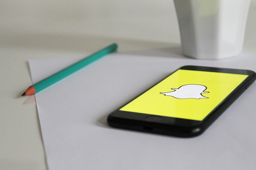 Ein Smartphone mit Snapchat liegt auf einem Blatt Papier neben einem Stift