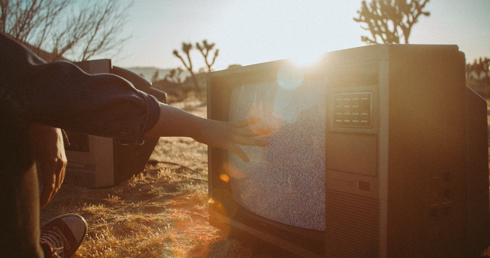 Ein alter Röhrenfernseher steht in der Wüste, eine Hand berührt den Bildschirm mit Störbild
