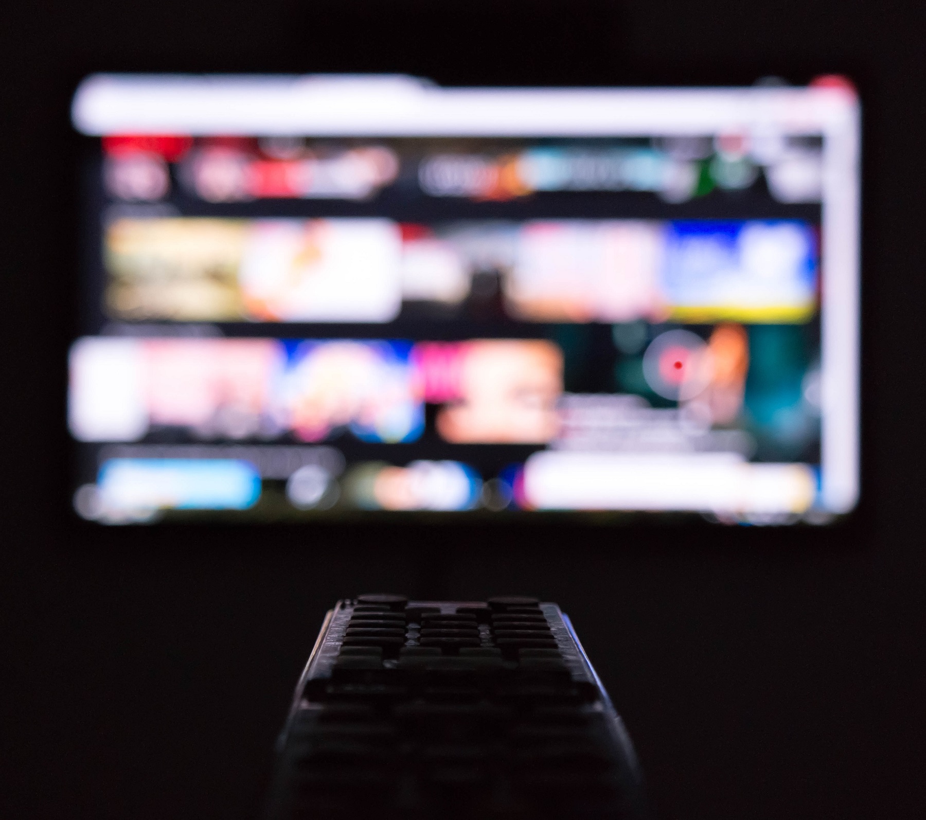 Im Hintergrund sieht man einen TV mit einer auf ihn gerichteten Fernbedienung