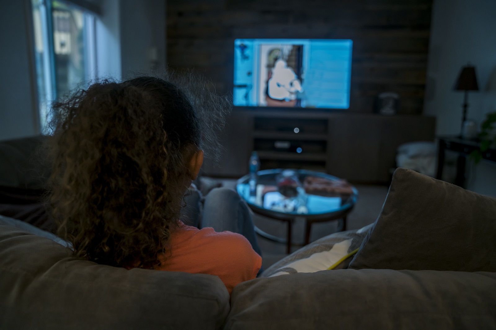 Ein Mädchen sitzt im Dunklen allein auf der Couch und guckt TV