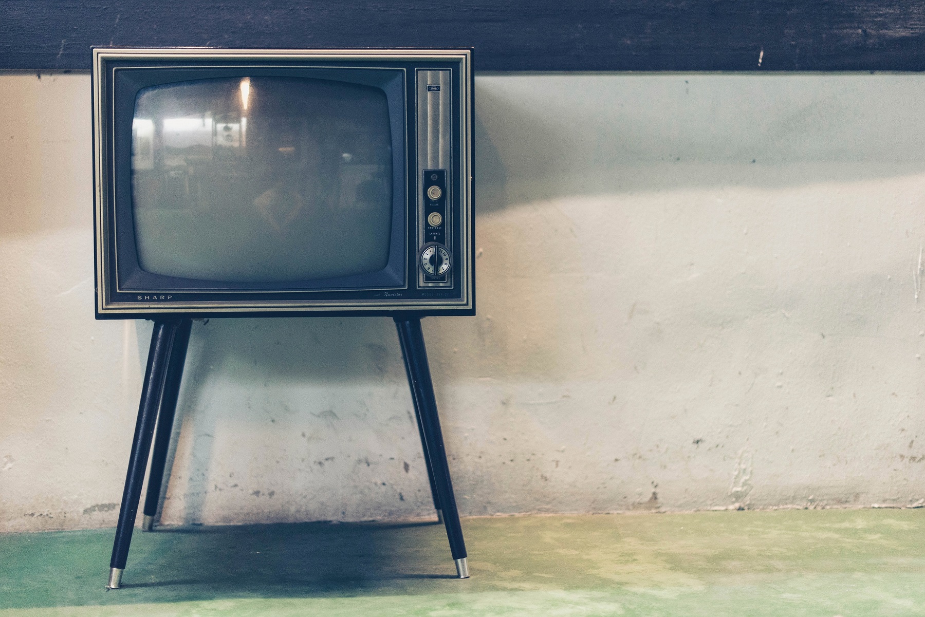 Alter Röhrenfernseher mit Beinen steht vor einer Betonwand