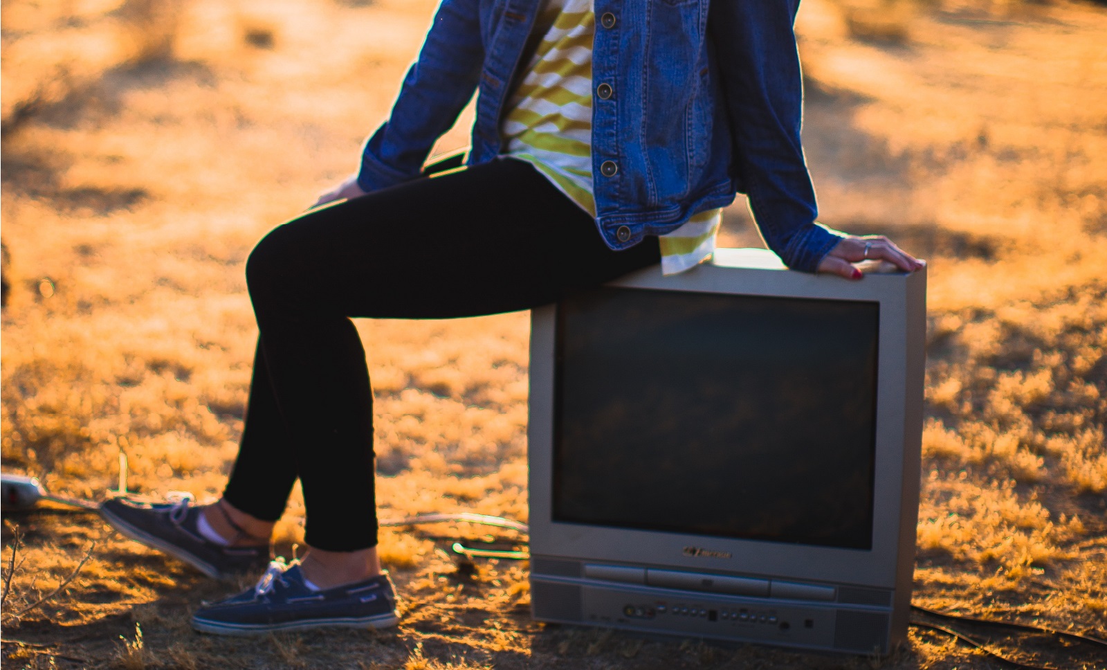 Ein Teenager sitzt auf einem alten Fernsehgerät in der Wüste