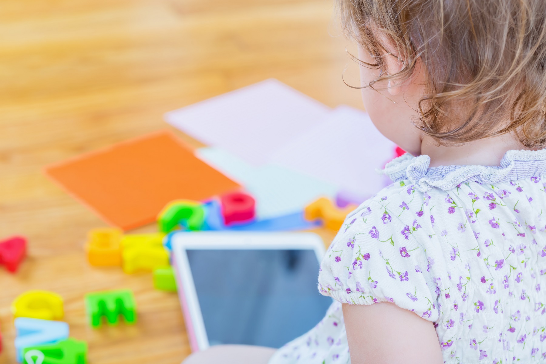 Hinterkopf und Rücken von Mädchen im Kindergartenalter, vor ihr auf dem Boden liegen ein Tablet und Bauklötze