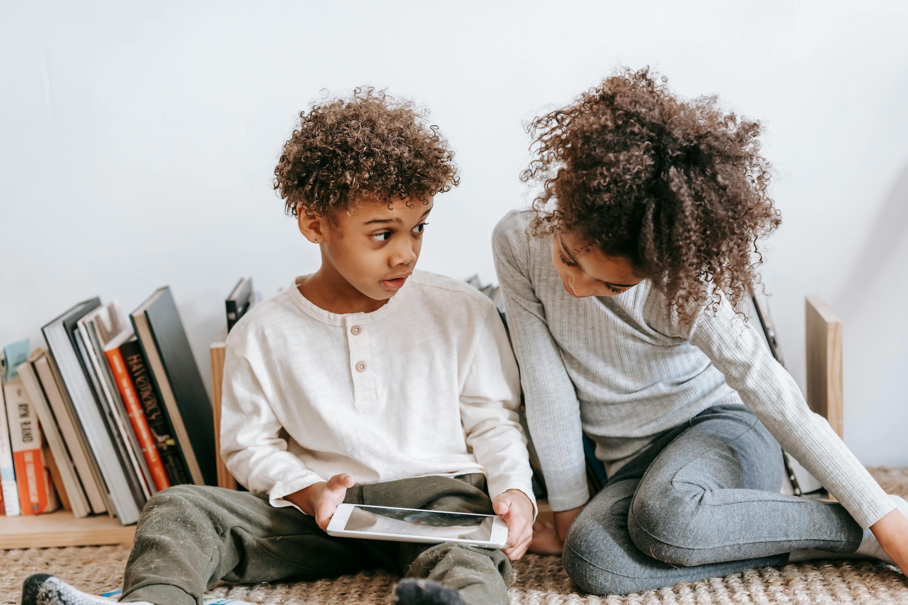 Zwei Kinder sitzen auf dem Boden und schauen in ein Tablet.
