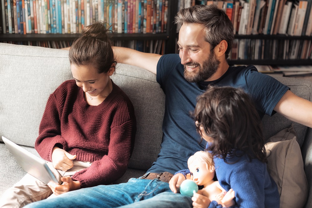 Ein Vater und seine zwei Töchter schauen gemeinsam auf ein Tablet